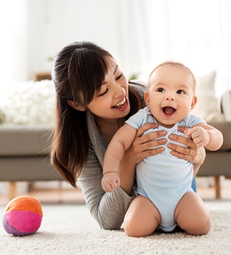 A mother holding her baby while playing in the floor in preparation for visiting a dental practice that offers dentistry for infants in Garland