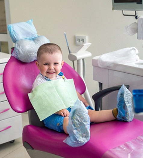 A little boy seated in a dentist’s chair and smiling before a general checkup