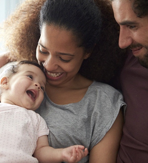 A mother and father holding their baby smiling at the infant’s expressions