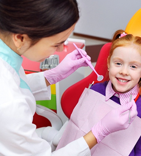 A young girl with red hair smiles while a dentist prepares to check her teeth during a regular checkup and cleaning appointment
