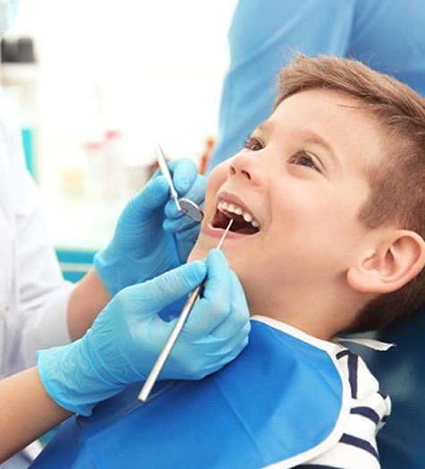 A young boy smiles while a dentist looks at the vacated socket in his mouth to determine if he needs a space maintainer
