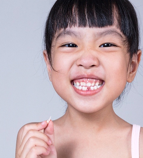 A little girl smiles while holding an extracted tooth that was removed from the lower arch of her mouth