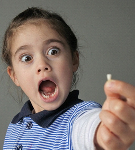 Shocked girl holds tooth removed by Garland pediatric dentist