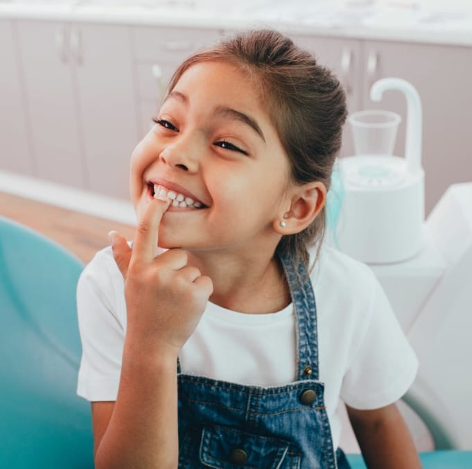 Young girl in dental chair pointing to her smile