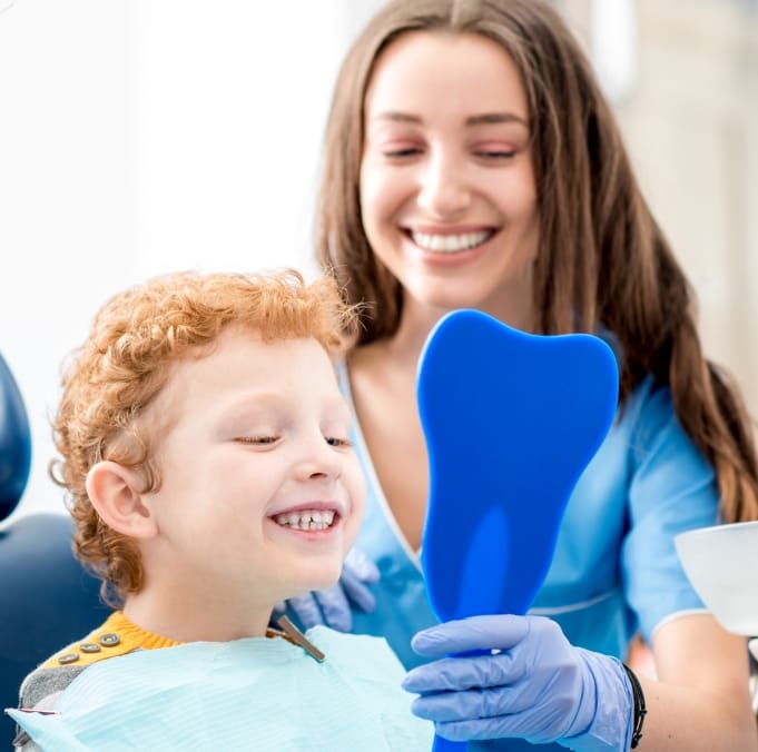 Little boy in dental chair looking at his smile in tooth shaped mirror