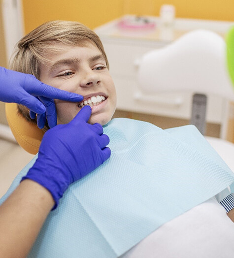 A dentist performing an oral cancer screening on a young, male teenager