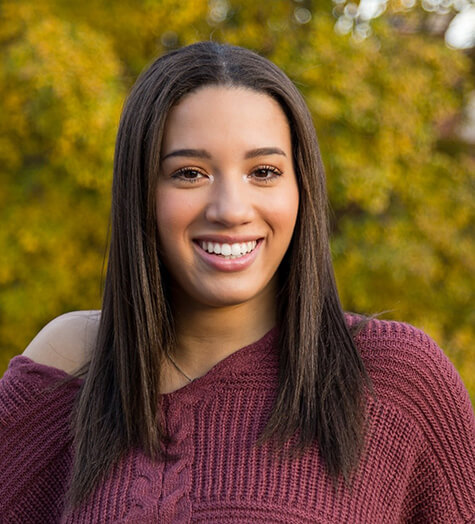 A female teenager wearing a purple sweater and smiling after receiving silver diamine fluoride treatment