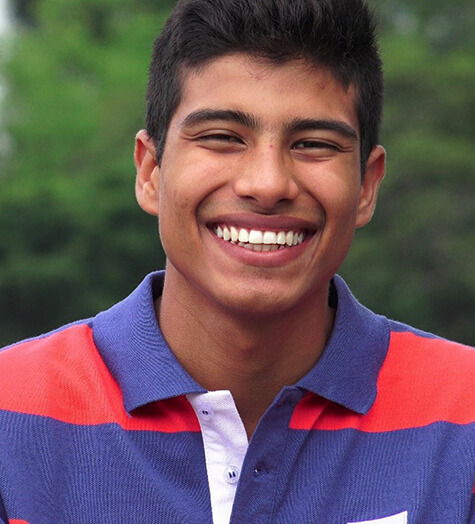 A male teen wearing a multi-colored polo shirt and smiling while standing outside