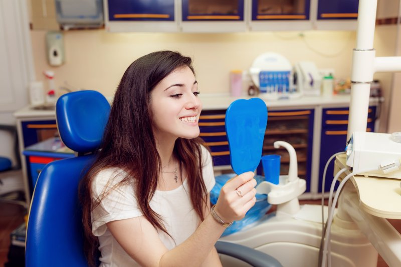 a teenage girl looks at her smile in the mirror while at the pediatric dentist’s office