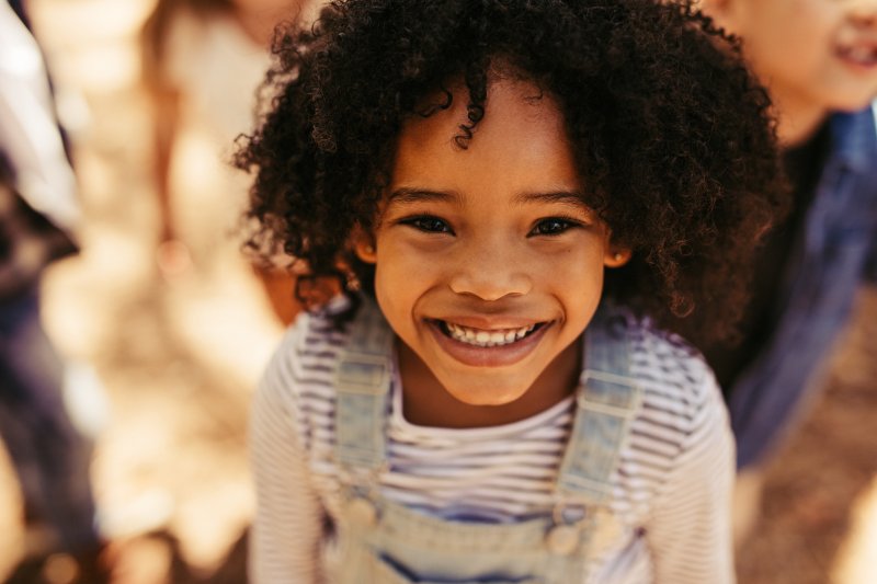 a little girl wearing denim overalls and showing off her healthy, beautiful smile