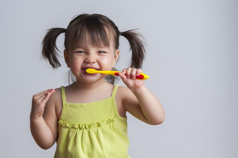 a little girl with pigtails using a manual toothbrush to clean her teeth