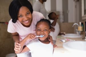 mother encouraging daughter brushing teeth 