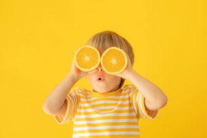 Little boy in a striped shirt holding orange slices over his eyes